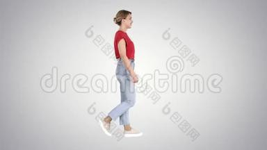 穿红色t恤，牛仔裤和运动鞋的女人在渐变背景下行走。